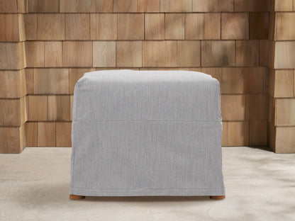 Three light gray Montego Outdoor Collection Covers: a sofa, armchair, and ottoman, on a patio with a wooden wall.