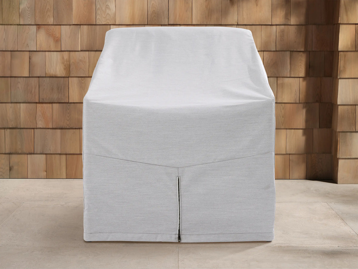 Light gray Montauk Outdoor Collection Cover on a chair, front view, with a vertical zipper, outdoor patio background.