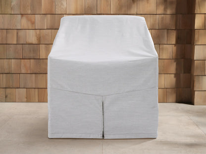 Light gray Montauk Outdoor Collection Cover on a chair, front view, with a vertical zipper, outdoor patio background.