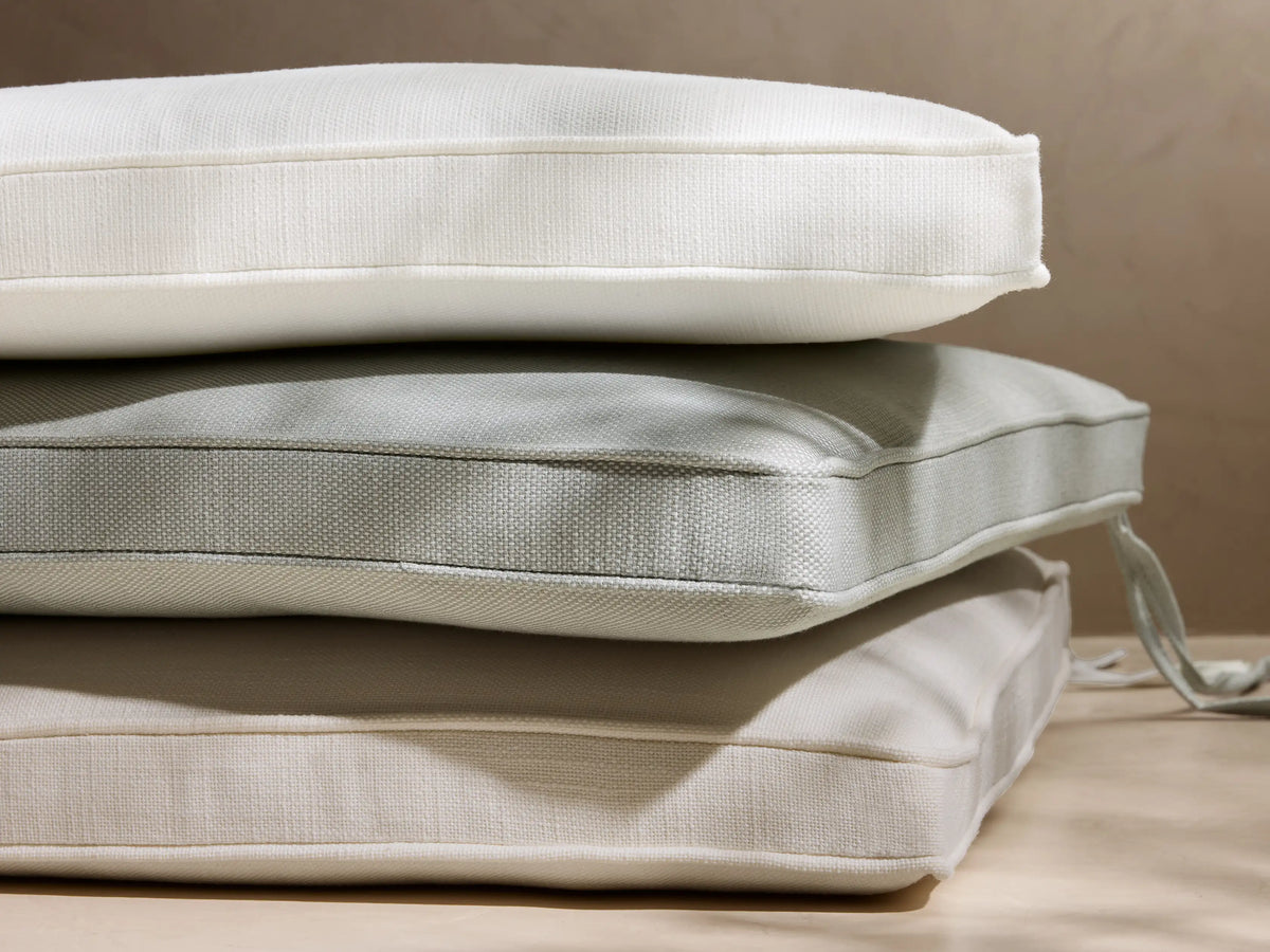 Stack of 3 Montauk outdoor water-repellent cushions: cream, sage green, beige, with textured fabric & piped edges, one with tie.