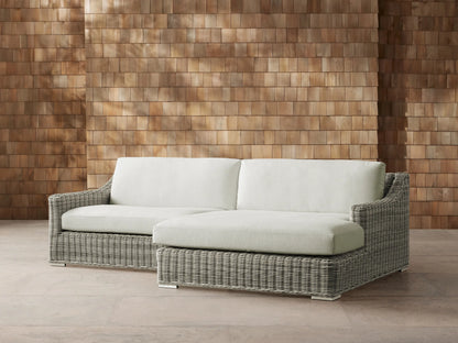 Montauk Outdoor Two-Piece Sectional with light gray woven resin wicker frame & pale green cushions against a wood wall.