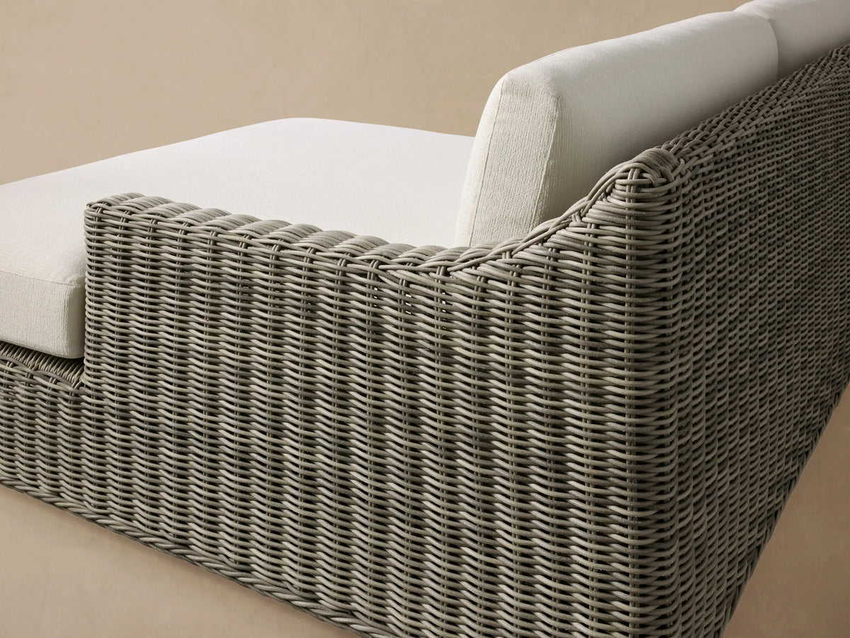 Montauk Outdoor Two-Piece Sectional with grey woven resin wicker base and cream cushions, on a patio against a shingled wall.