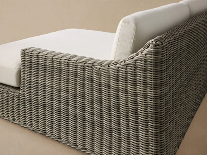 Montauk Outdoor Two-Piece Sectional with grey woven resin wicker base and cream cushions, on a patio against a shingled wall.