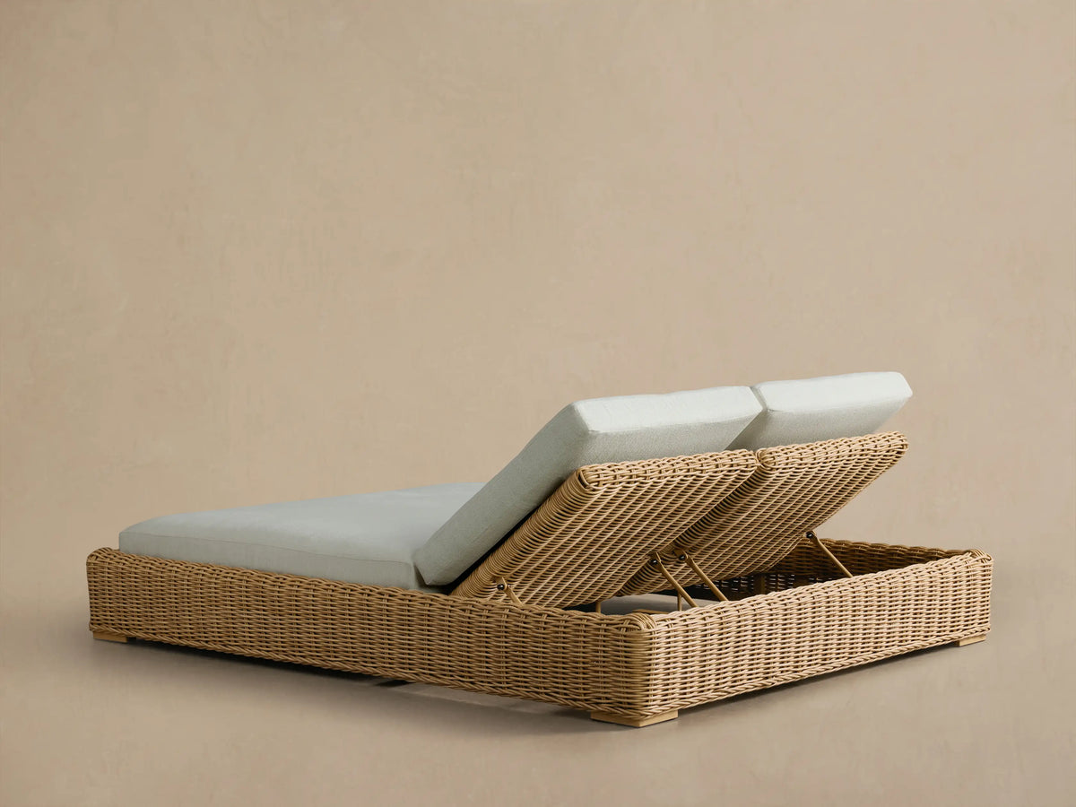Side view of the Montauk Outdoor Double Chaise, featuring natural woven wicker and light gray cushions with an elevated headrest.