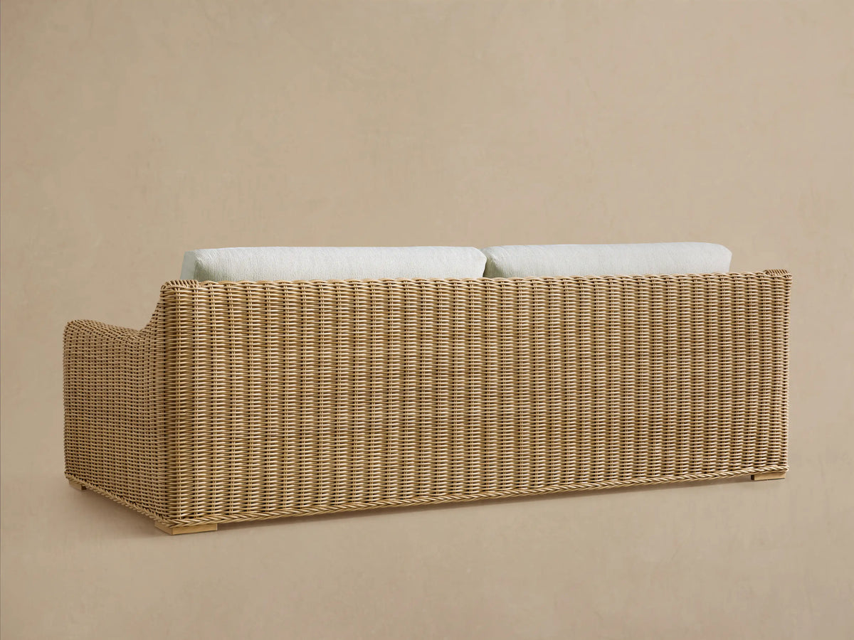 Rear view of the Montauk Outdoor Sofa, featuring natural handwoven resin wicker and light cream cushions peeking over the back.