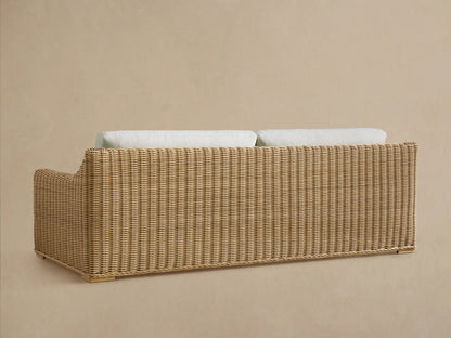 Rear view of the Montauk Outdoor Sofa, featuring natural handwoven resin wicker and light cream cushions peeking over the back.