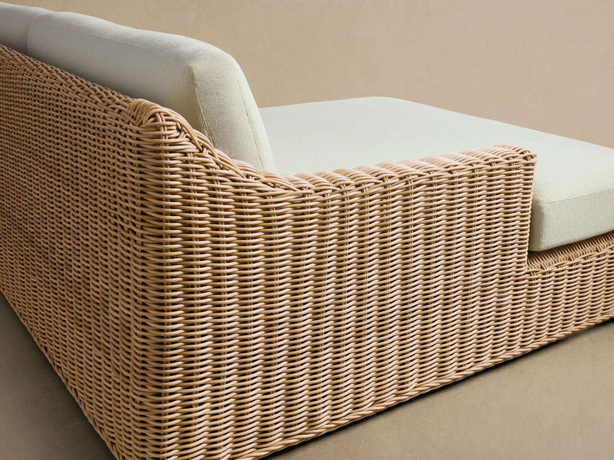 Montauk Outdoor Two-Piece Sectional, light brown woven resin wicker frame with cream cushions on a patio, shingle wall background.