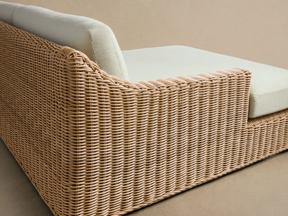 Montauk Outdoor Two-Piece Sectional, light brown woven resin wicker frame with cream cushions on a patio, shingle wall background.
