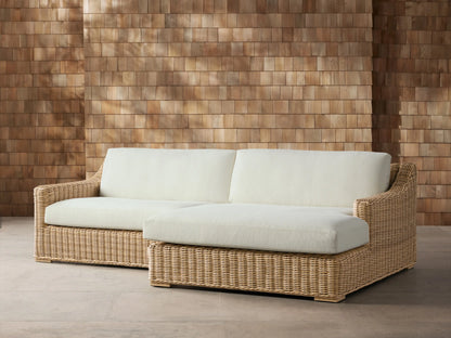 Montauk Outdoor Two-Piece Sectional: Light brown woven wicker, cream cushions, against a textured wooden wall.