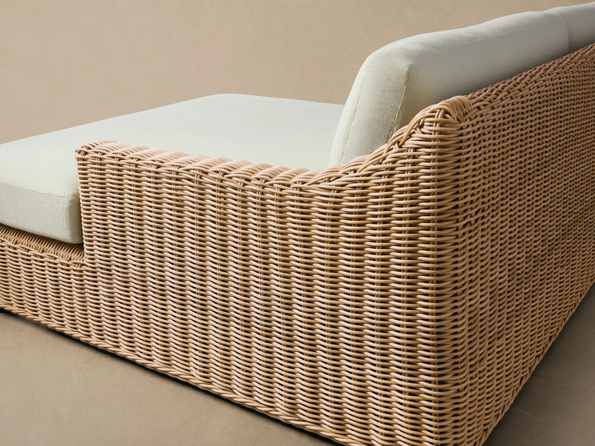 Montauk Outdoor Two-Piece Sectional with natural woven wicker and light cream cushions on a patio against a wooden wall.