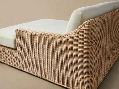 Montauk Outdoor Two-Piece Sectional with natural woven wicker and light cream cushions on a patio against a wooden wall.