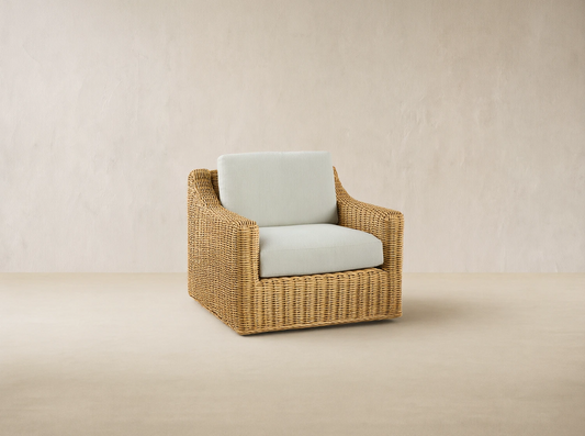 Montauk Outdoor Swivel Chair, light tan woven resin wicker with cream cushions, viewed from front-right on a patio.