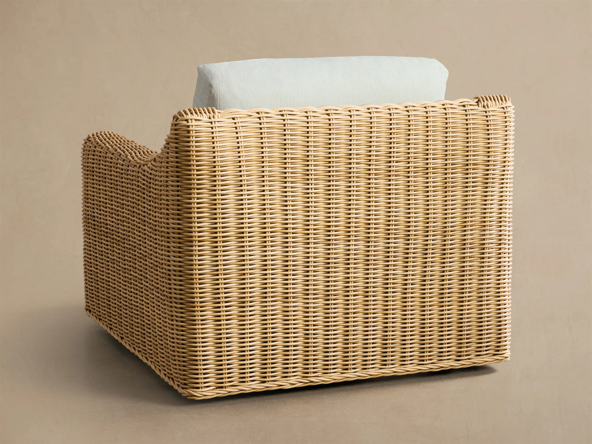 Close-up, angled view of Montauk Outdoor Swivel Chair, showing light brown woven resin wicker frame and light grey cushions.