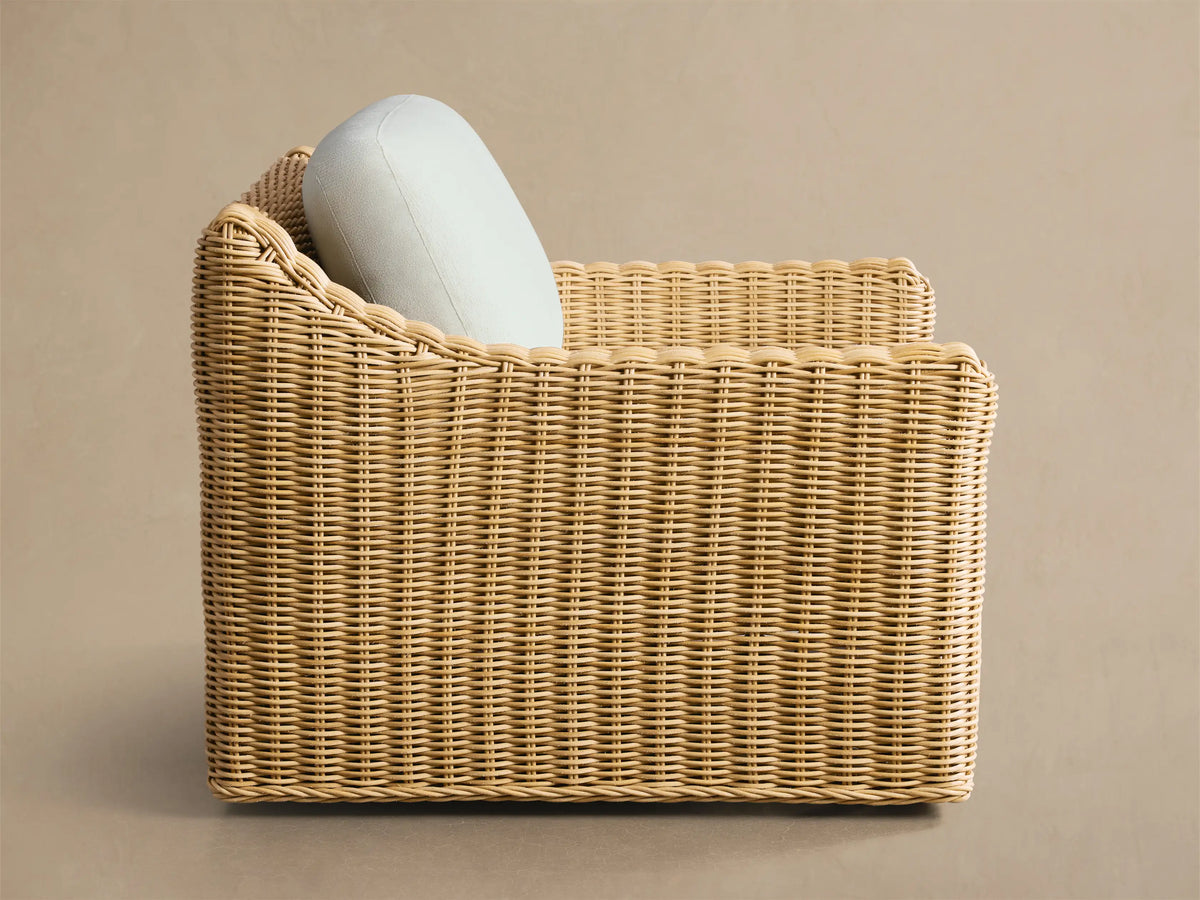 Montauk Outdoor Swivel Chair, back-right view, handwoven light tan all-weather resin wicker with a light blue cushion.