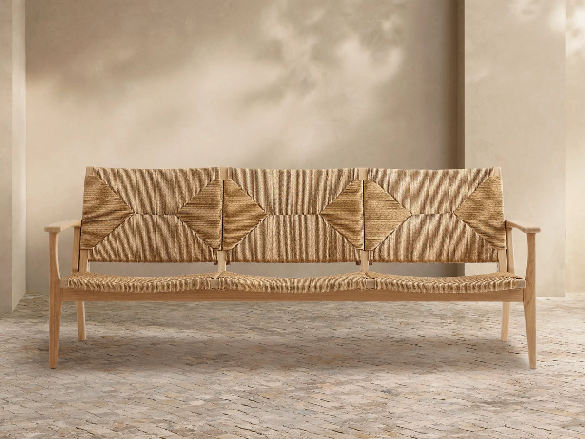 Mustique Outdoor Sofa with light teak wood frame, woven beige backrest with diamond patterns, & seat, on stone patio.