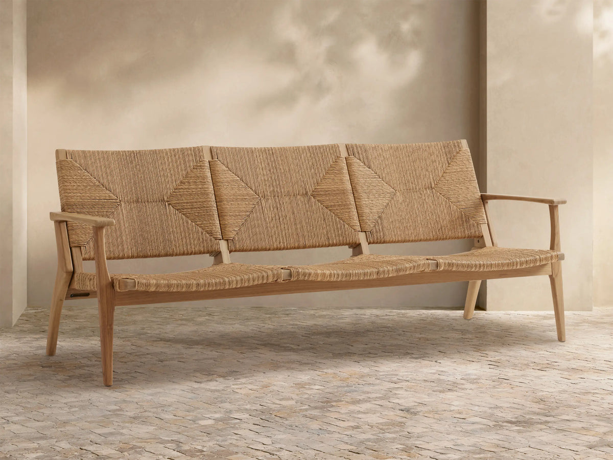 Mustique Outdoor Sofa with light teak wood frame, woven beige backrest with diamond patterns, & seat, on stone patio.