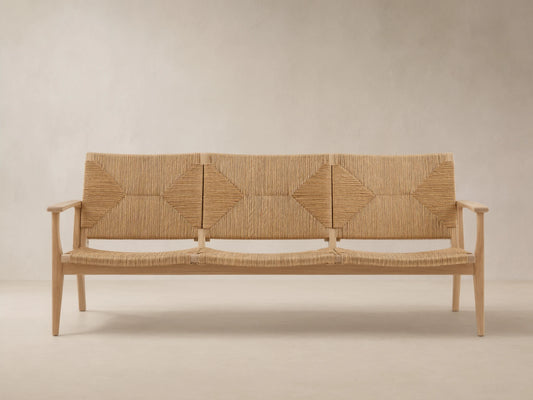 Mustique Outdoor Sofa with light teak wood frame, woven beige backrest with diamond patterns, & seat, on stone patio.