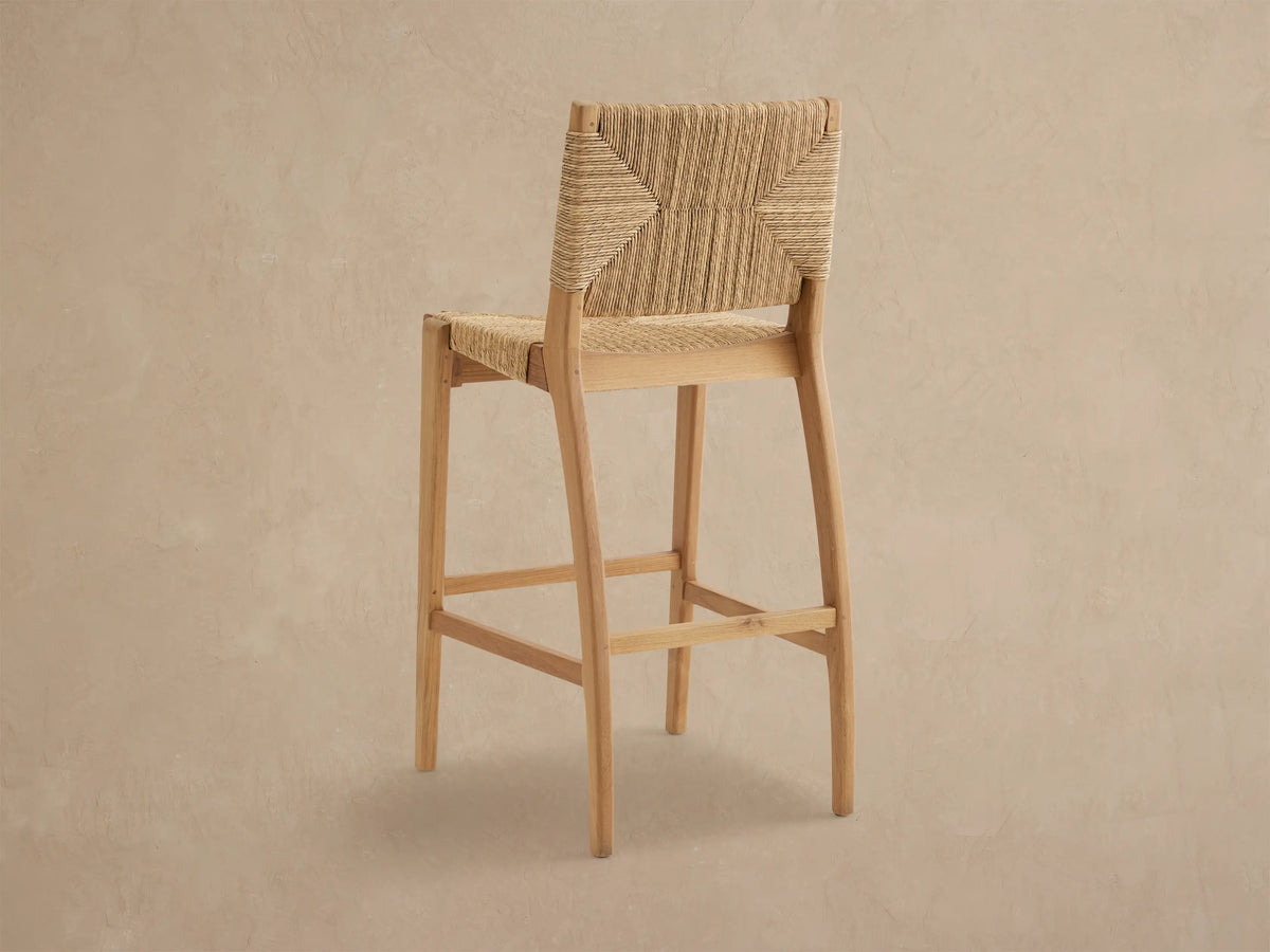 Close-up of Mustique Outdoor Barstool's textured, woven light brown backrest & seat on a natural teak frame.