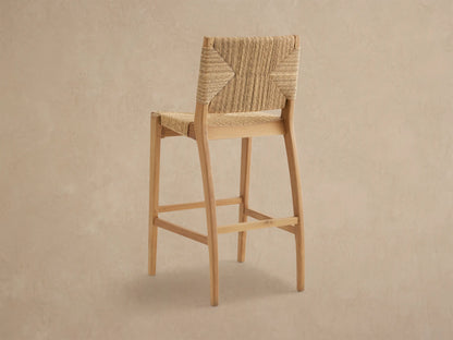 Close-up of Mustique Outdoor Barstool's textured, woven light brown backrest & seat on a natural teak frame.