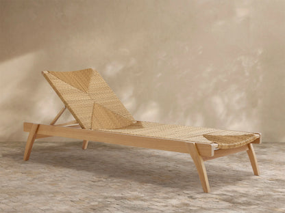 Mustique Outdoor Chaise, light teak frame, natural woven seat & angled backrest with geometric pattern, on paved patio.