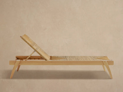 Mustique Outdoor Chaise, light teak frame, natural woven seat & angled backrest with geometric pattern, on paved patio.
