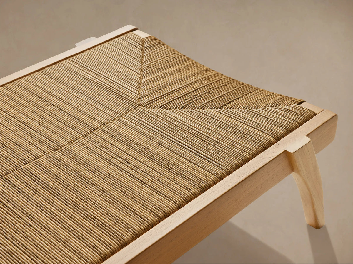Mustique Outdoor Chaise, side view. Golden teak frame with natural woven beige wicker seat and an angled backrest on light background.