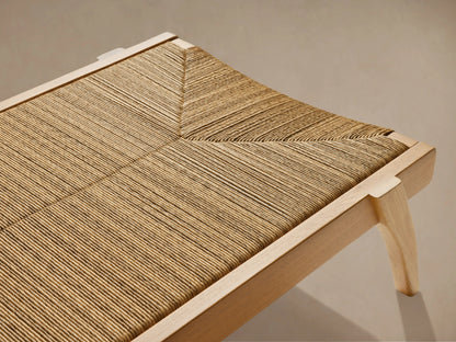 Mustique Outdoor Chaise, side view. Golden teak frame with natural woven beige wicker seat and an angled backrest on light background.