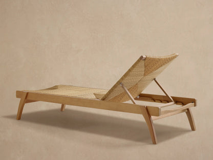 Close-up of Mustique Outdoor Chaise, showing its light teak frame and woven natural-colored seat with a V-pattern.