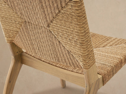 Mustique Outdoor Dining Side Chair, natural teak frame with woven beige wicker back & seat, facing front on a stone floor.