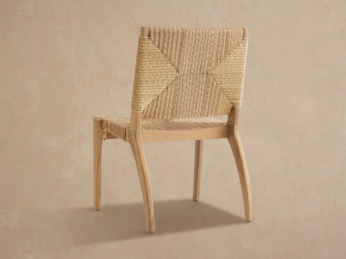 Mustique Outdoor Dining Side Chair, angled. Light teak frame with intricately woven tan wicker backrest and seat.