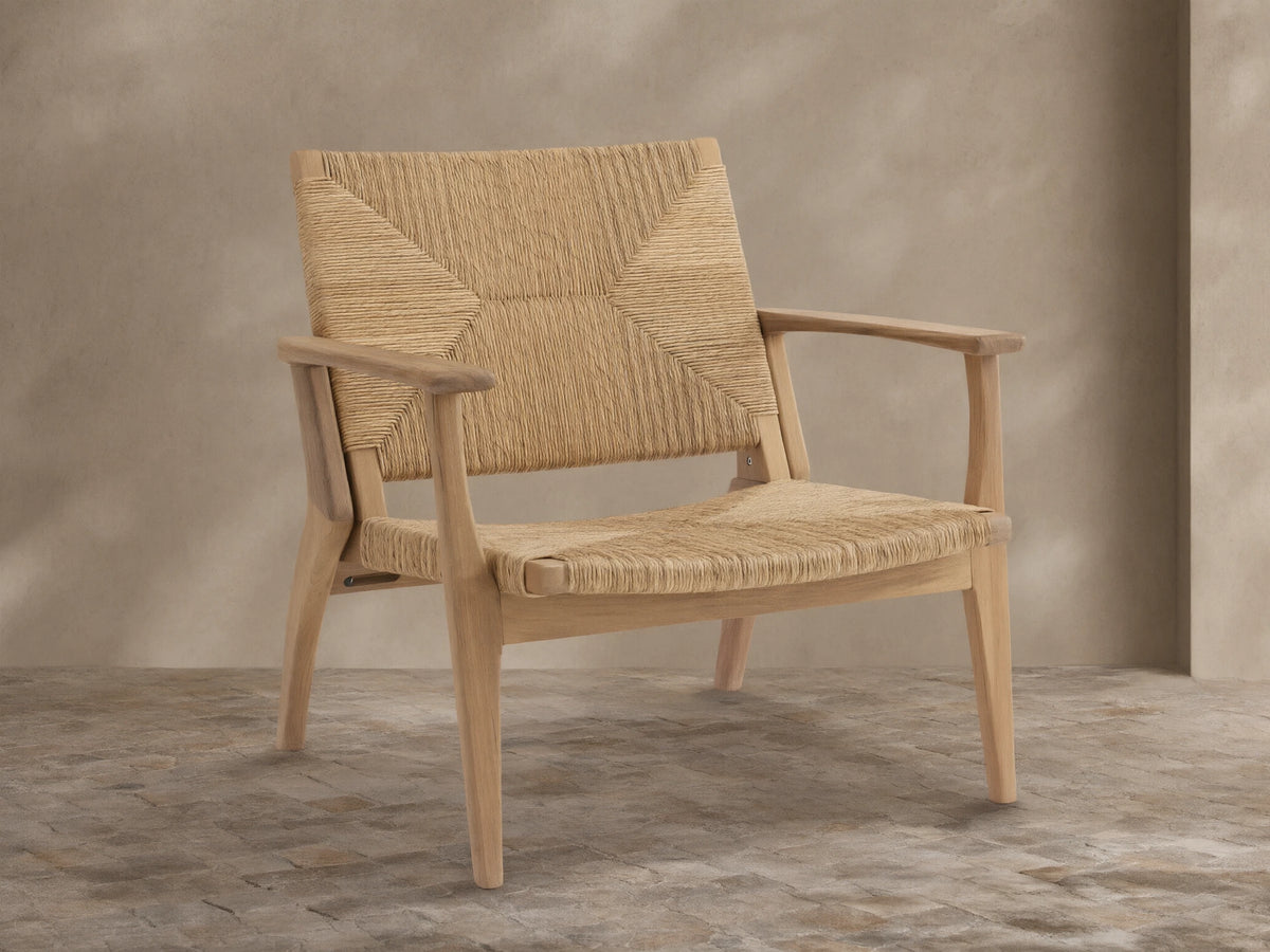 Mustique Outdoor Lounge Chair, light golden teak frame with natural woven wicker seat & back, front-facing on tiled patio.