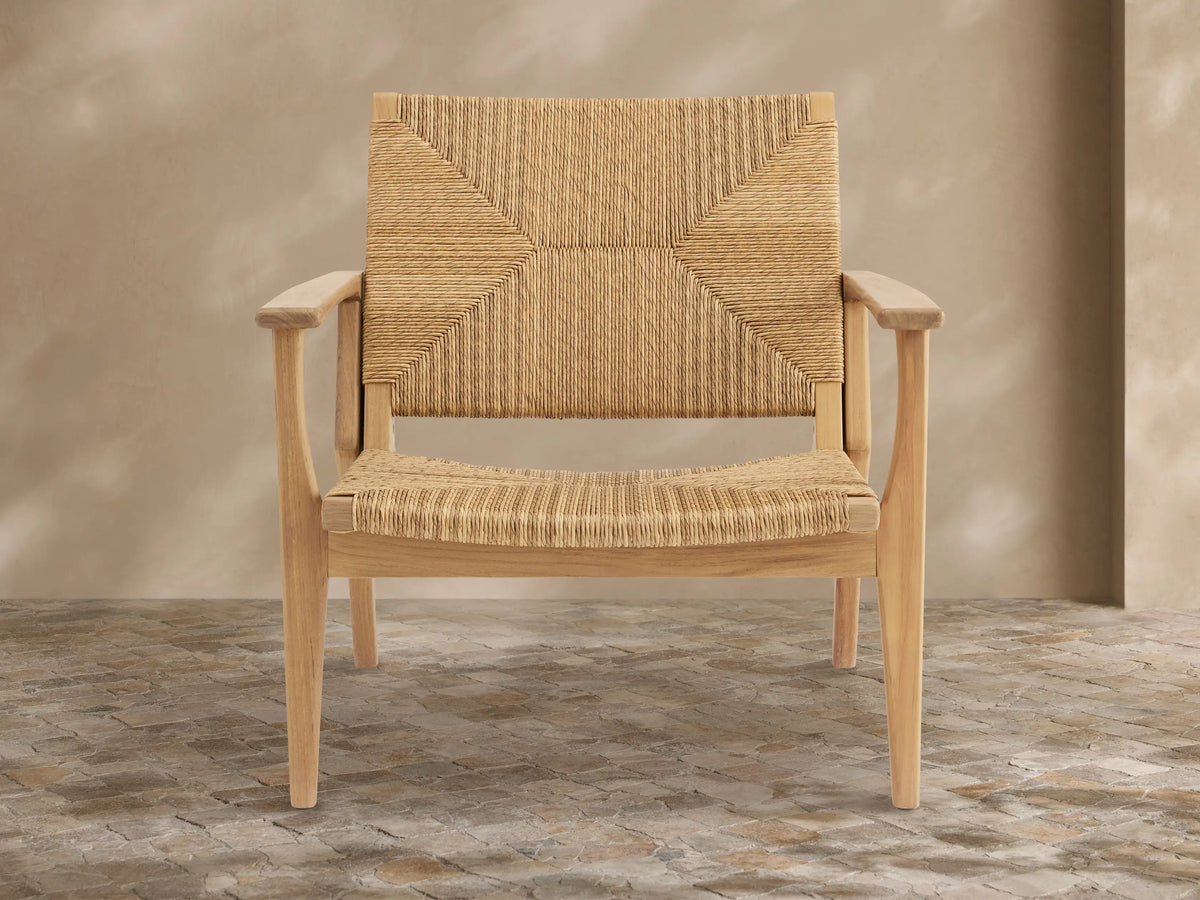 Mustique Outdoor Lounge Chair, light golden teak frame with natural woven wicker seat & back, front-facing on tiled patio.