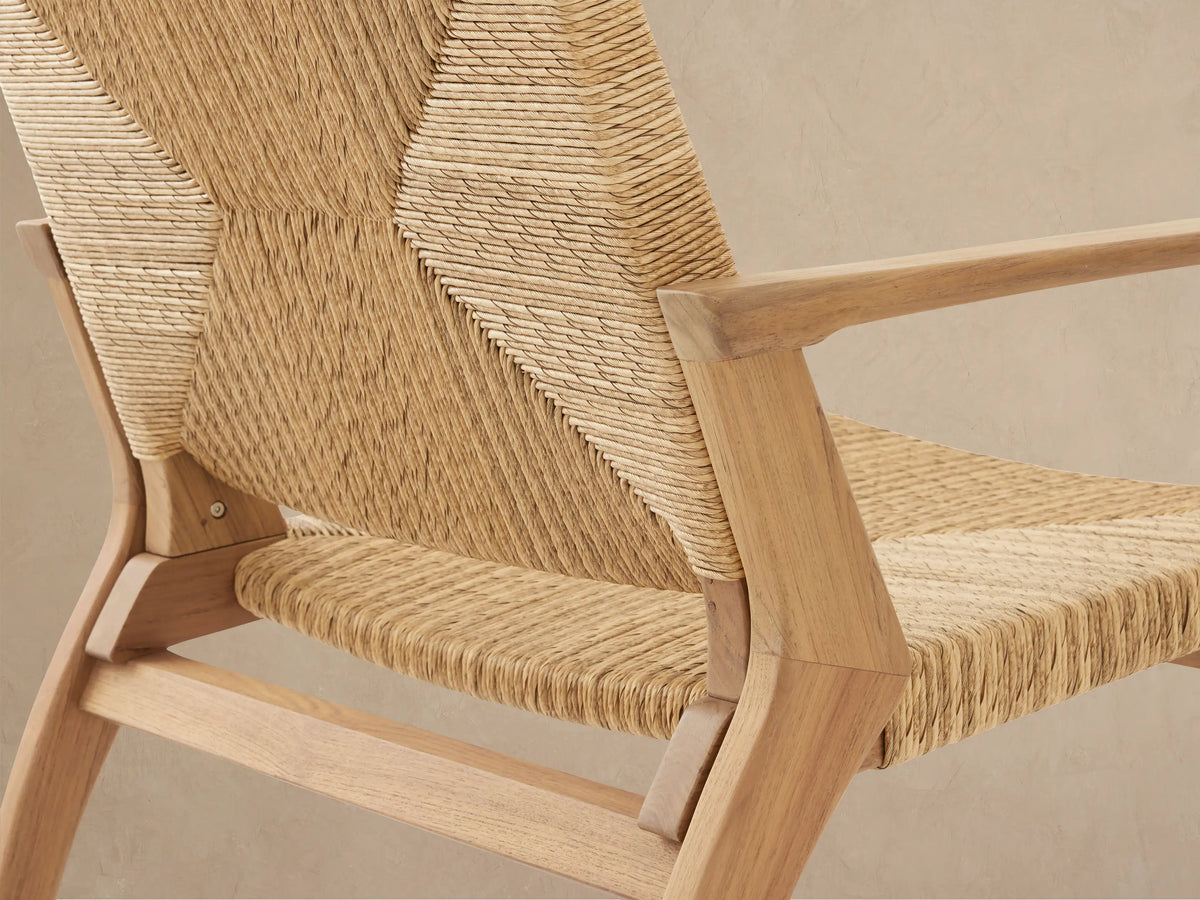 Front view of Mustique Outdoor Lounge Chair, light teak frame & woven tan wicker with chevron pattern, on a patio.