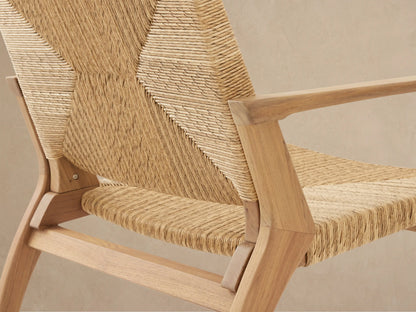 Front view of Mustique Outdoor Lounge Chair, light teak frame & woven tan wicker with chevron pattern, on a patio.
