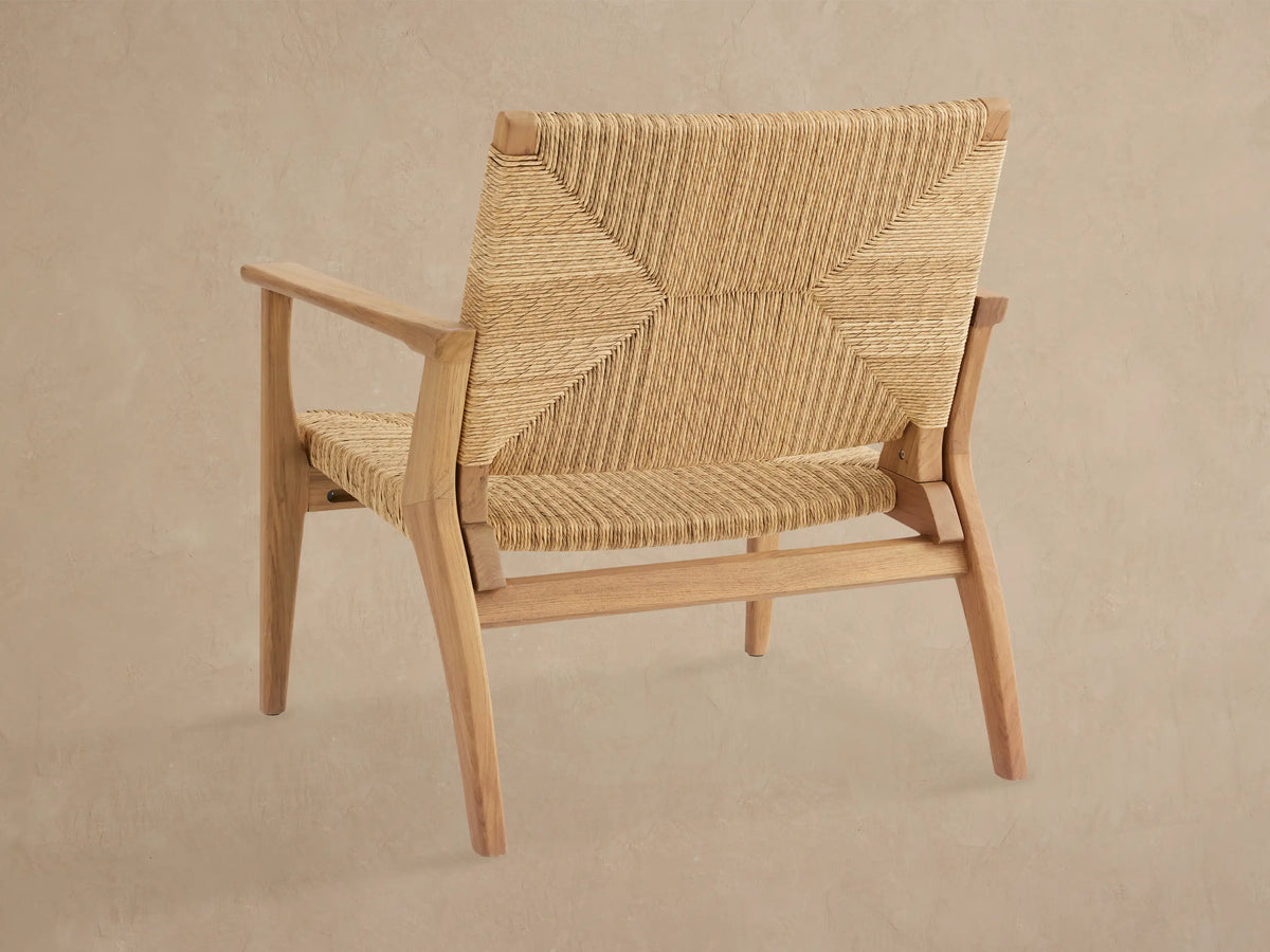 Close-up of a Mustique Outdoor Lounge Chair, angled view. Light-toned teak wood frame with woven natural beige wicker back & seat.