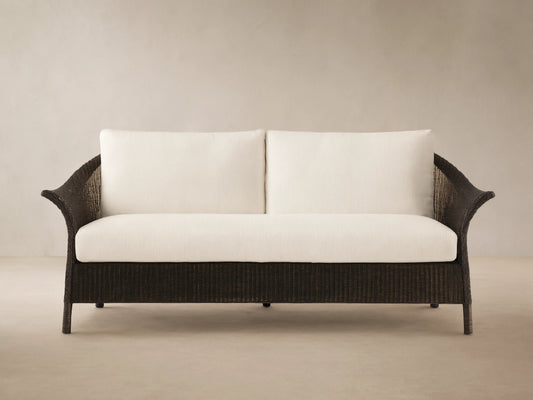 Nantucket Sunroom Sofa with dark brown woven rattan frame and white Eden Snow cushions, in a sunroom against a tan wall.
