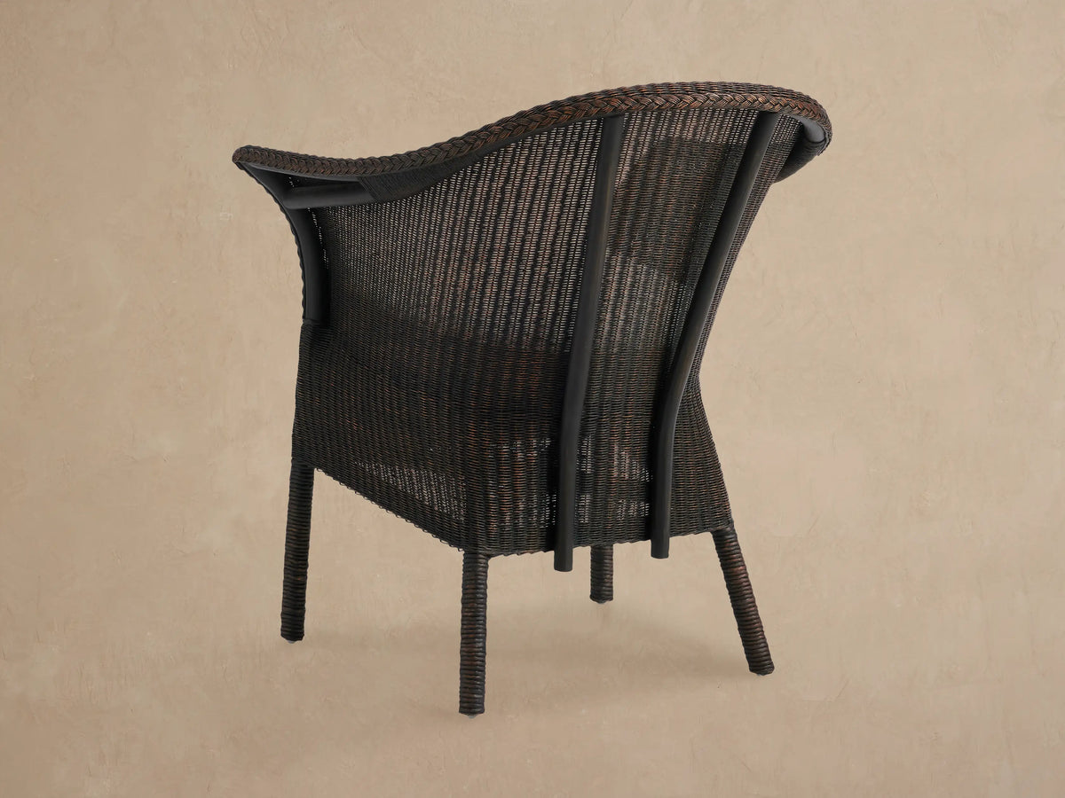 Close-up of Nantucket Sunroom Dining Arm Chair, dark brown woven rattan with braided arm detail and light cream seat cushion.