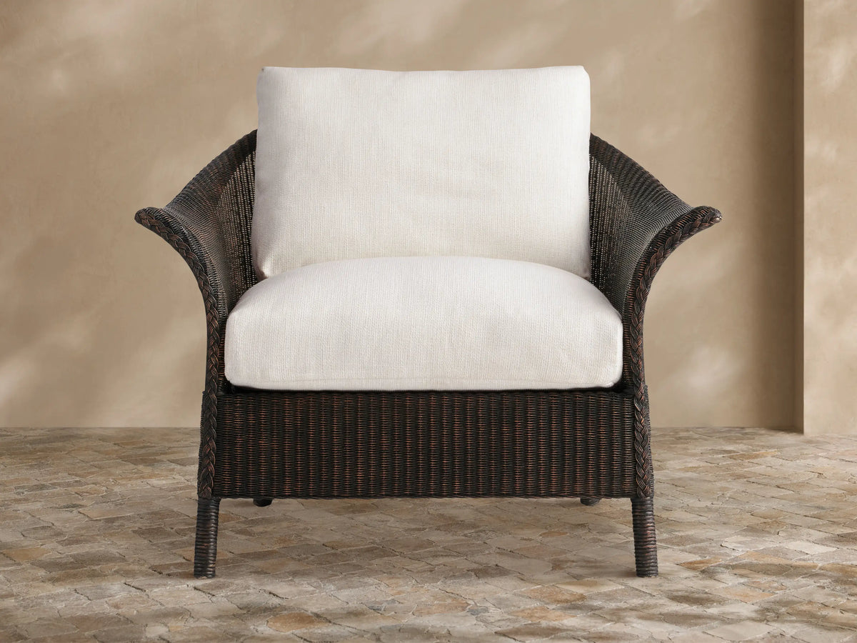 Dark brown woven Nantucket Sunroom Lounge Chair with thick white cushions, angled on a stone patio against a beige wall.