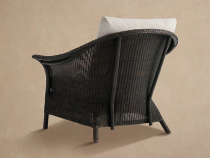 Angled close-up of Nantucket Sunroom Lounge Chair. Dark brown woven rattan armrest with braided edge, cream seat cushion.