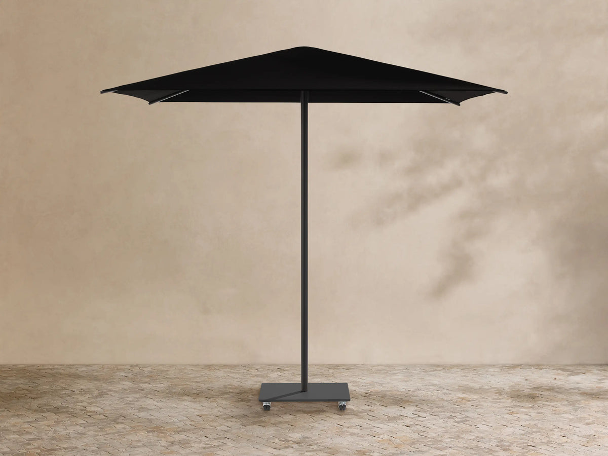 Black Nata Outdoor Square Umbrella with a square canopy, central pole, and wheeled base, against a tan wall and stone floor.