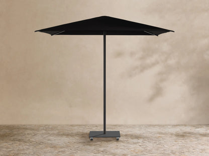 Black Nata Outdoor Square Umbrella with a square canopy, central pole, and wheeled base, against a tan wall and stone floor.
