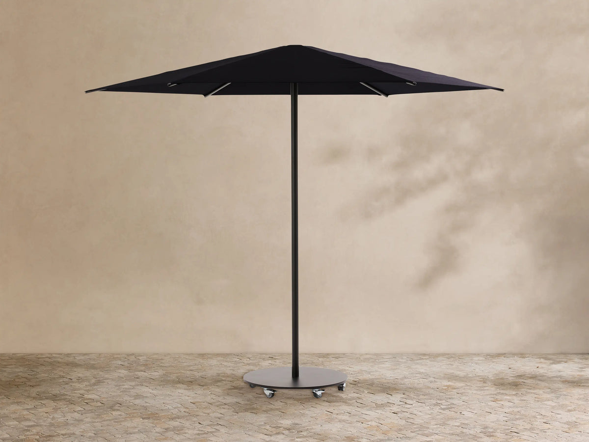 Black Nata Outdoor Round Umbrella, fully open, with a tall pole and dark grey wheeled base, on textured outdoor flooring.