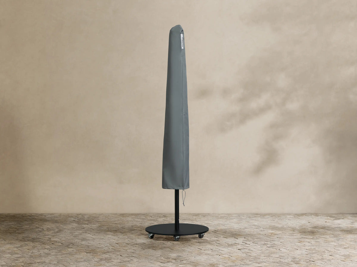 Black Nata Outdoor Round Umbrella, fully open, with a tall pole and dark grey wheeled base, on textured outdoor flooring.