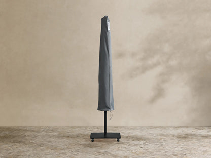 Nata Outdoor Square Scalloped Umbrella, closed. White canopy with black trim, black pole and wheeled base on a patio.
