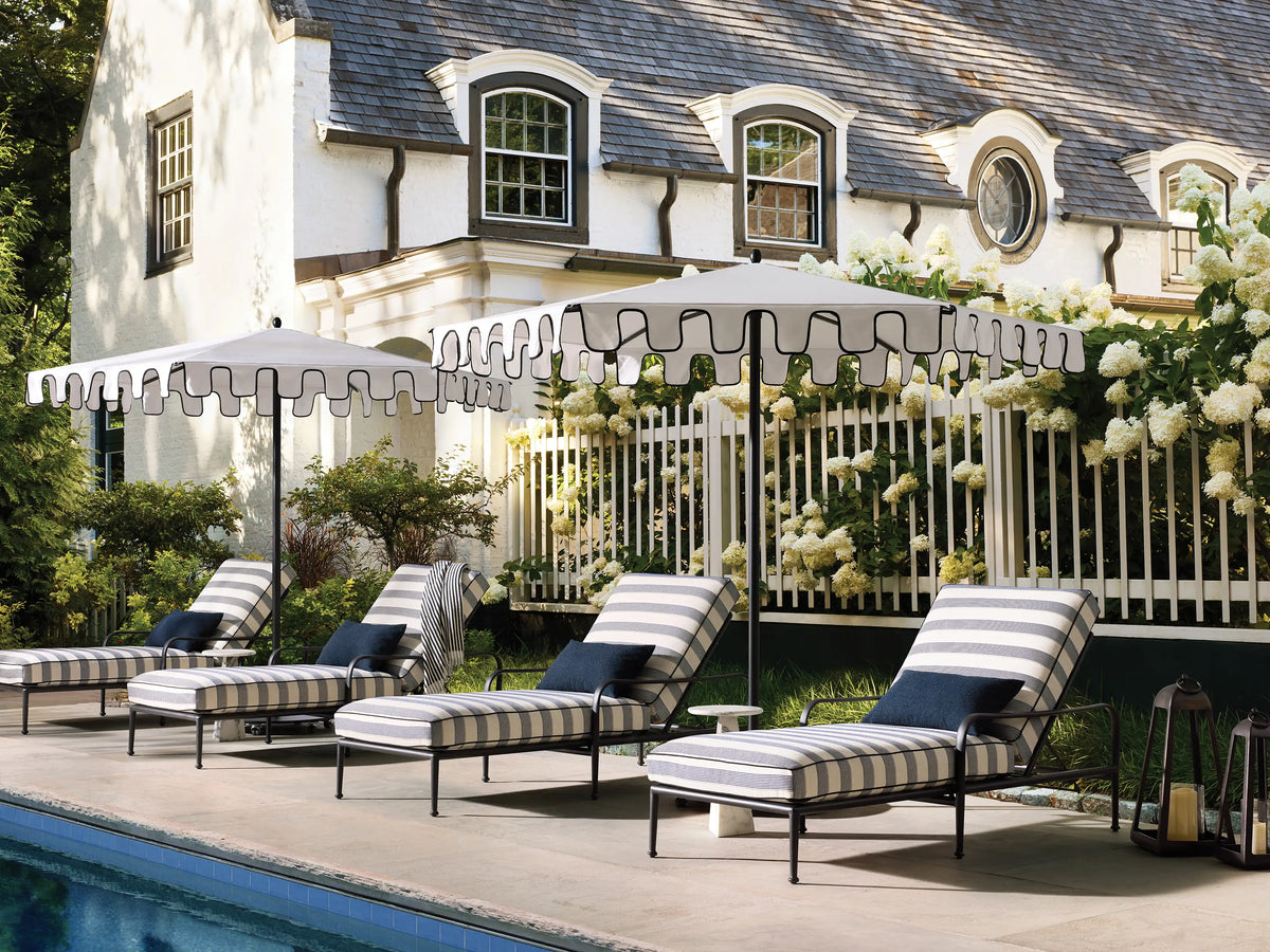 White Nata Outdoor Round Scalloped Umbrella with black trim, pole, and wheeled base, on a textured floor.