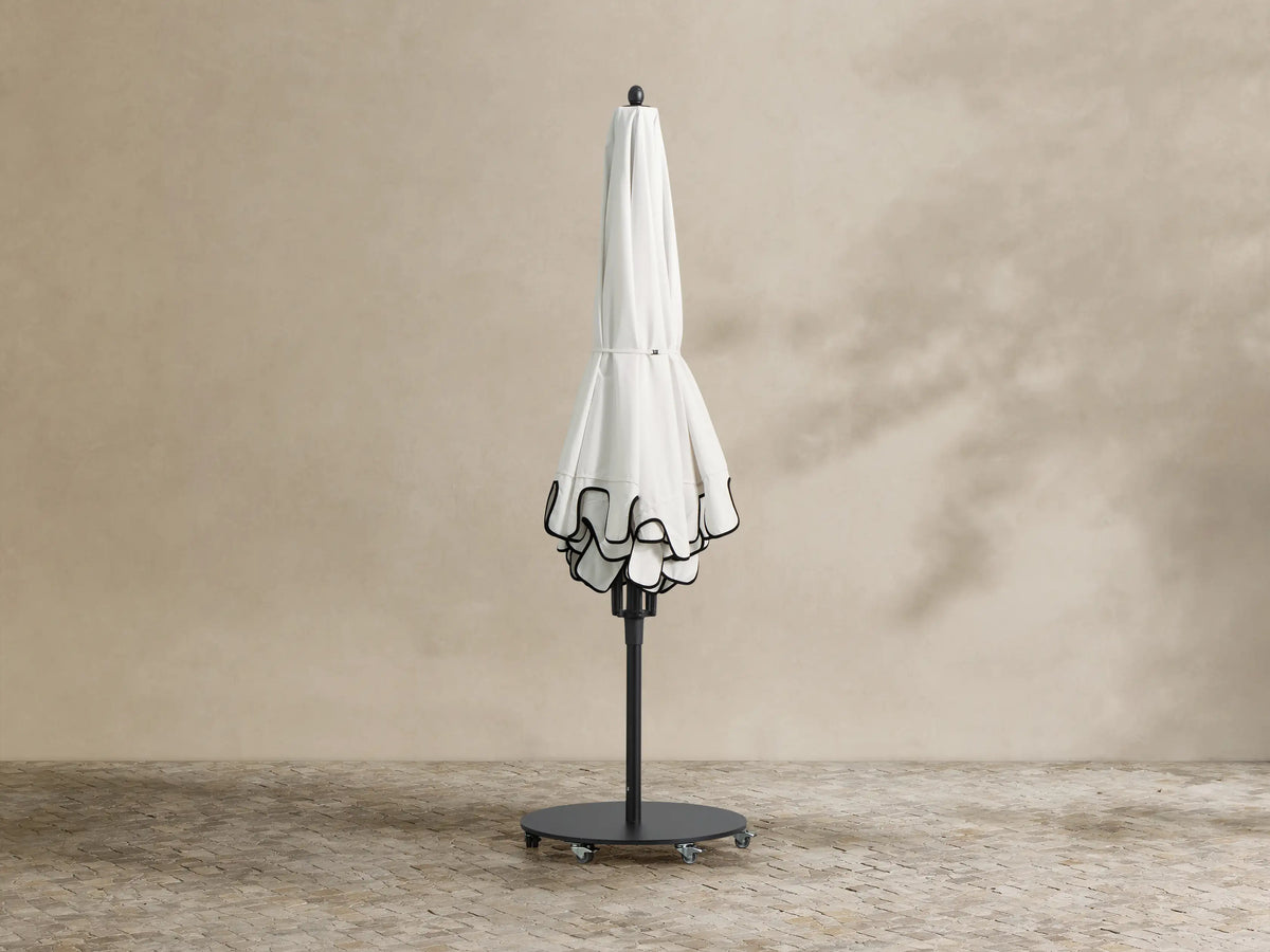 White Nata Outdoor Scalloped Umbrella with black scalloped trim opened over poolside lounge chairs.