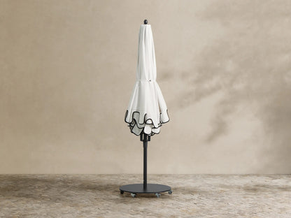 White Nata Outdoor Scalloped Umbrella with black scalloped trim opened over poolside lounge chairs.