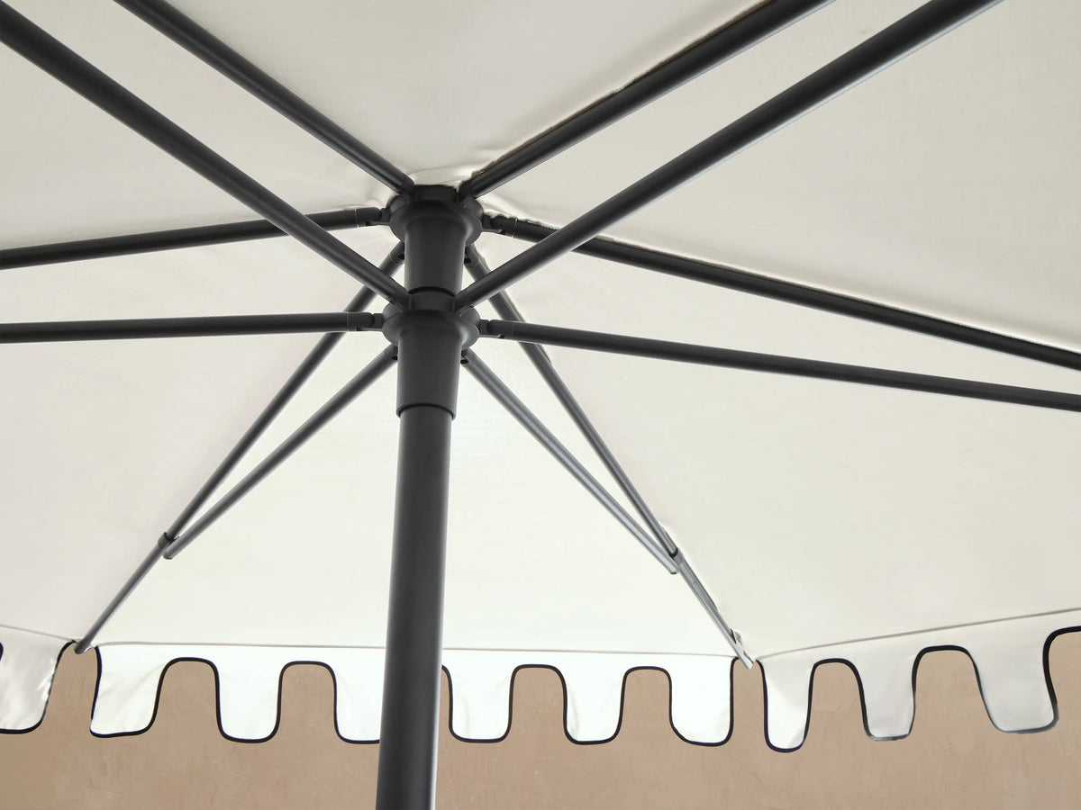 White Nata Outdoor Round Scalloped Umbrella canopy from an angle, showing black trimmed scalloped edge and black top finial.
