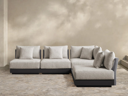 Naxos L-shaped outdoor sectional, light gray woven cushions, dark gray base, on a light tiled patio, against a beige wall.