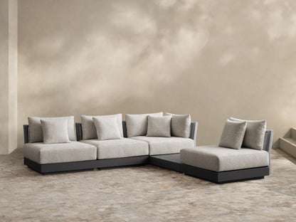 Naxos L-shaped outdoor sectional, light gray woven cushions, dark gray base, on a light tiled patio, against a beige wall.